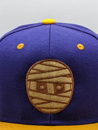 SNAPBACK CON CABEZA DE GOMA MORADO / DORADO